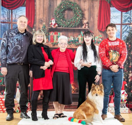 Family portrait in festive attire, with a dog, in a decorated holiday setting.